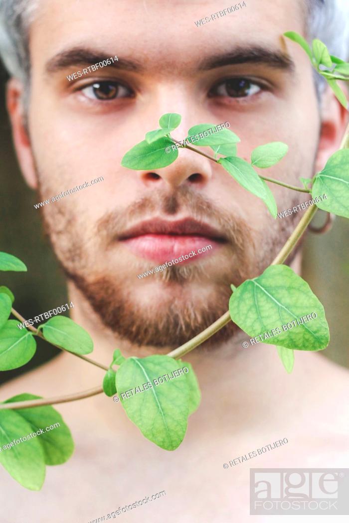 Stock Photo: Portrait of young man behind fern leaves twigs of honeysuckle.