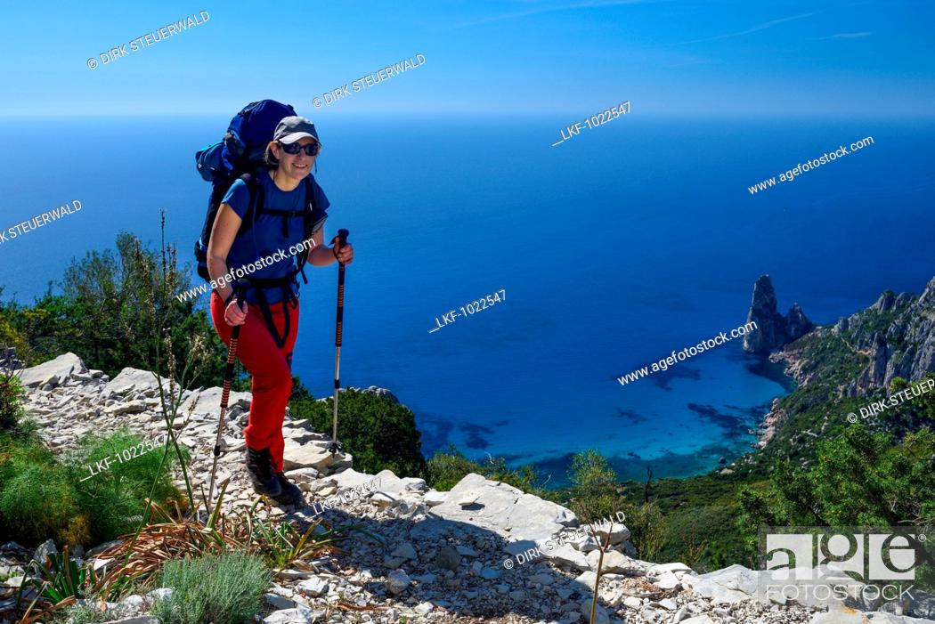 Stock Photo: A young woman hiking along the mountainous coast, rock-needle near Pedra Longa in the background, Selvaggio Blu, Sardinia, Italy, Europe.