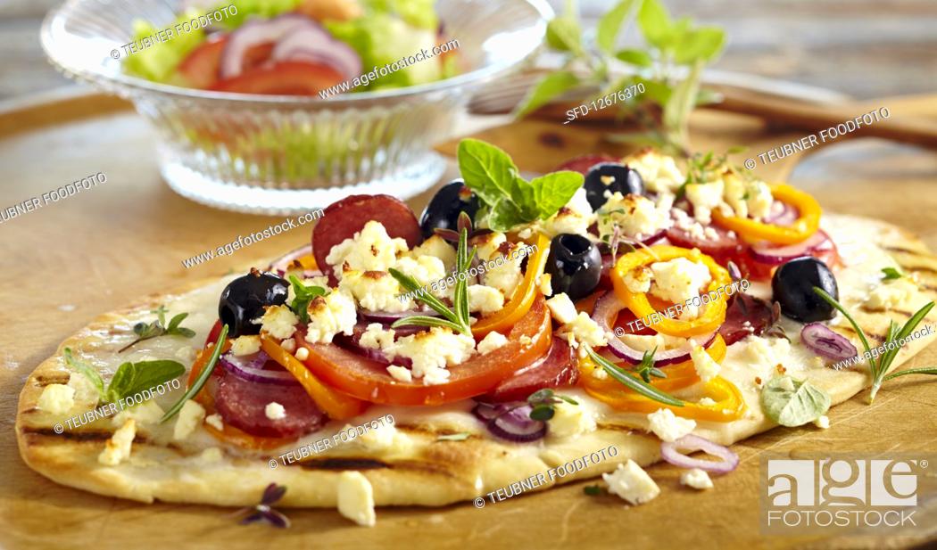Stock Photo: Grilled pizza topped with sausage, feta cheese, olives, peppers and fresh herbs.