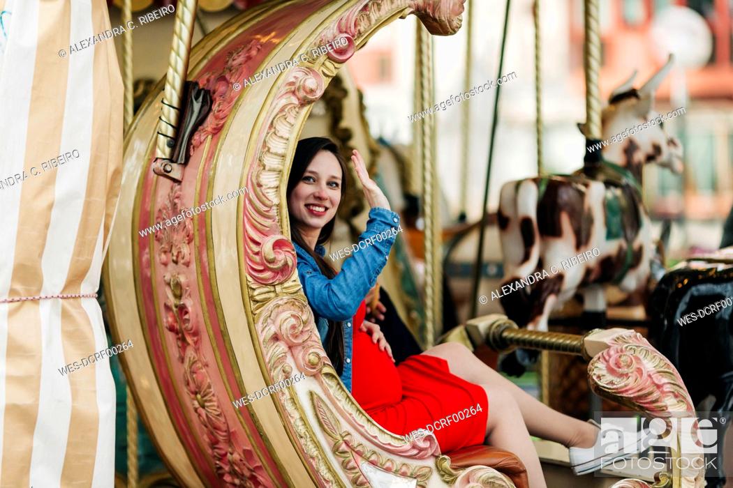 Stock Photo: Happy pregnant woman waving while sitting on carousel at amusement park, Cascais, Portugal.