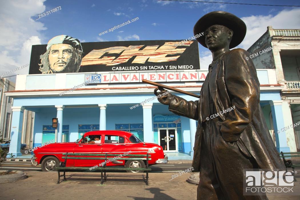 Stock Photo: View to the Benny More statue, one of the important musician and maestro of the Cuban music history, with the Che Guevara poster and an old American car at the.