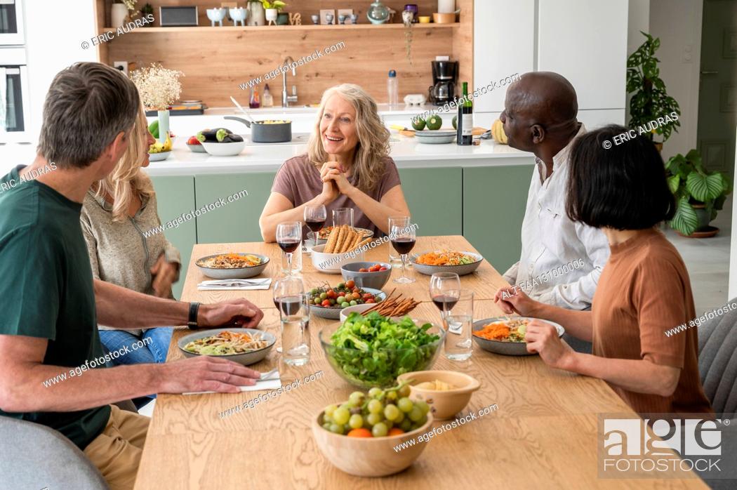 Stock Photo: Group of diverse middle-aged friends sharing stories while having lunch at home.