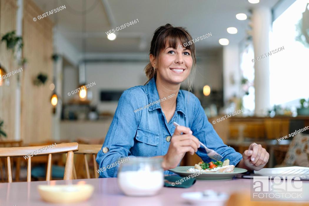 Stock Photo: Female owner eating food while sitting in cafe.