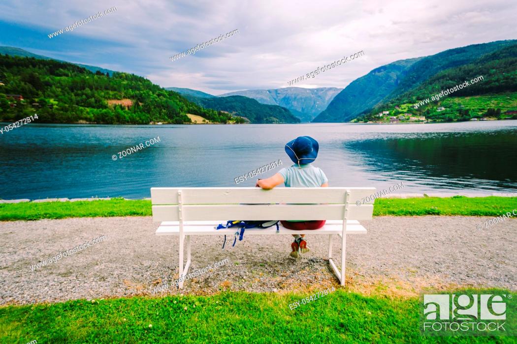 Stock Photo: Woman sitting on a bench looking at the fjord in Ulvik, Norway. Fjord coastal promenade in Ulvik, Hordaland county, Norge.