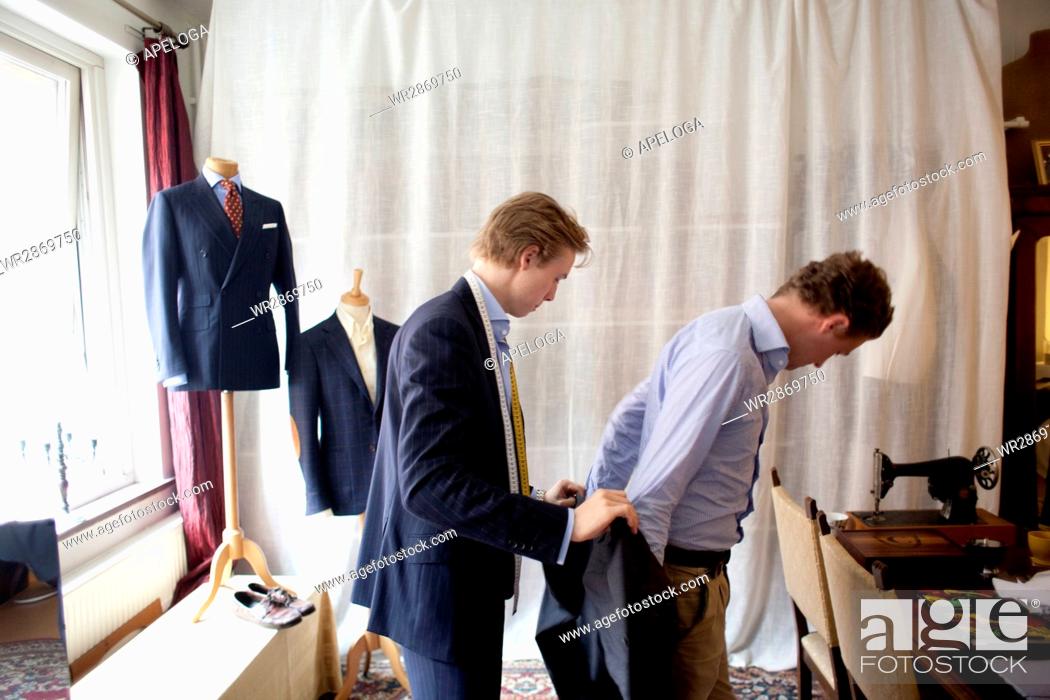 Imagen: Side view of tailor assisting man for wearing suit.