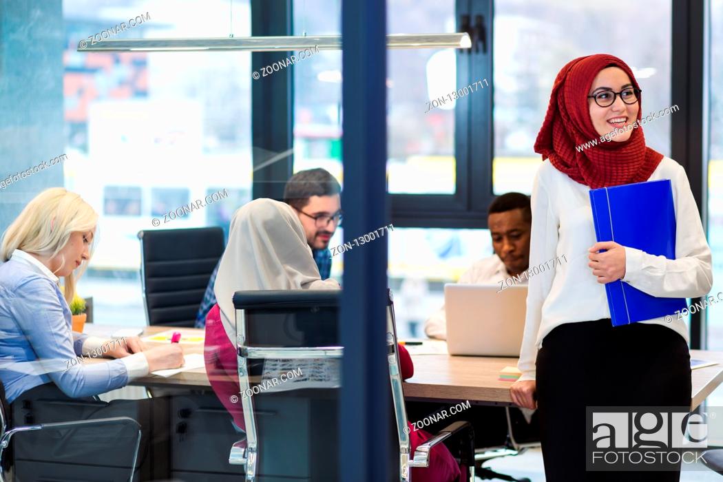 Stock Photo: Arabian Businesswoman in office with Businesspeople meeting in the background, Arabian woman wearing Hijab in office with her colleagues in background.