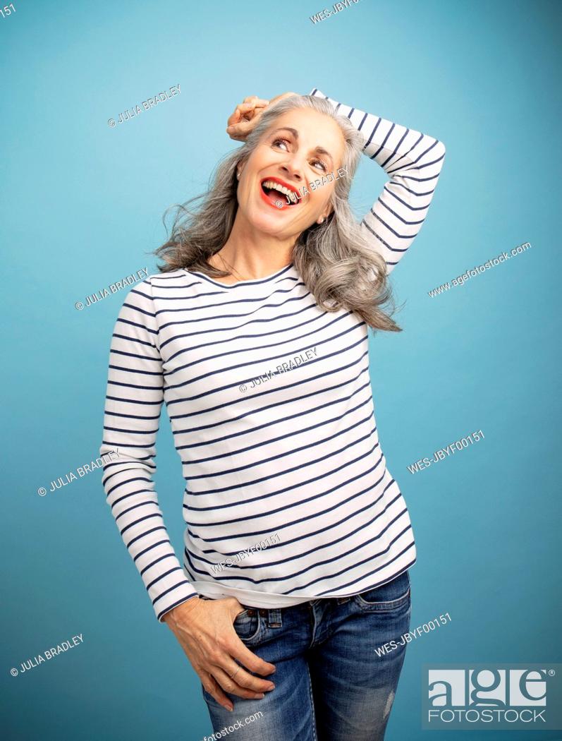 Stock Photo: Cheerful woman with hand on head standing against blue background.
