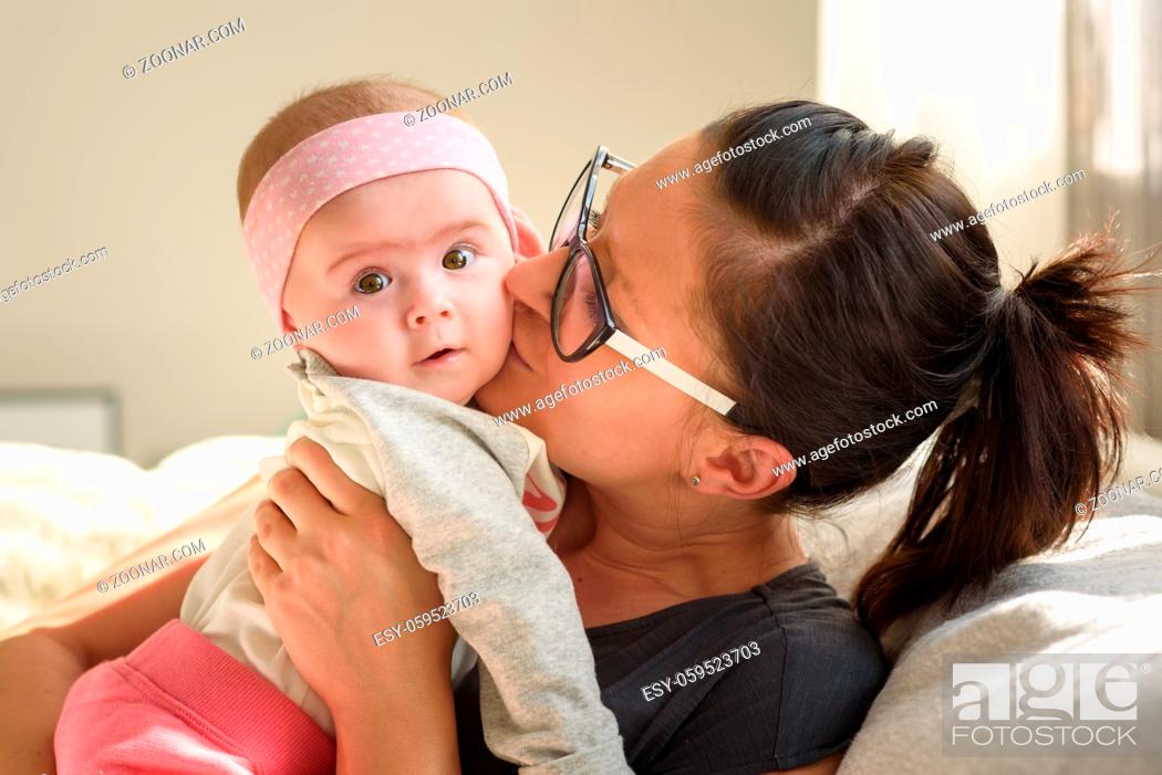 Stock Photo: Mother holding and kissing beautiful baby girl in bright sunny room. Motherhood background.