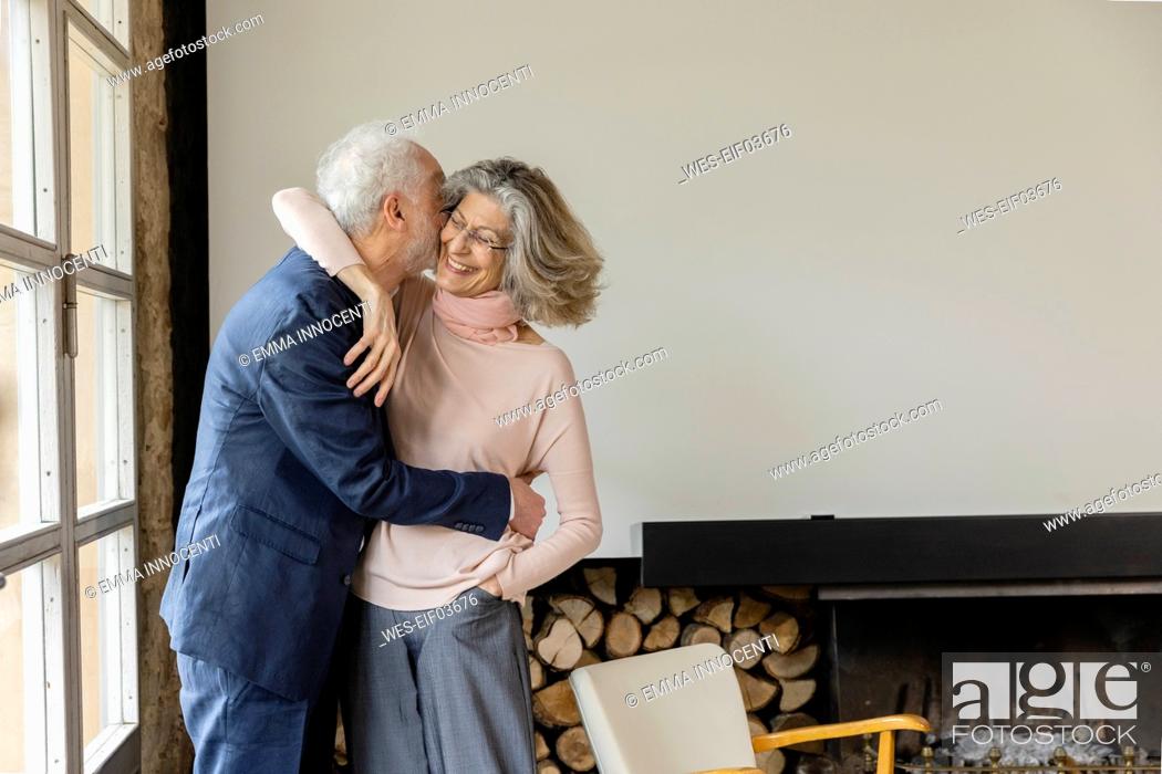 Stock Photo: Man kissing woman standing by window in living room at home.