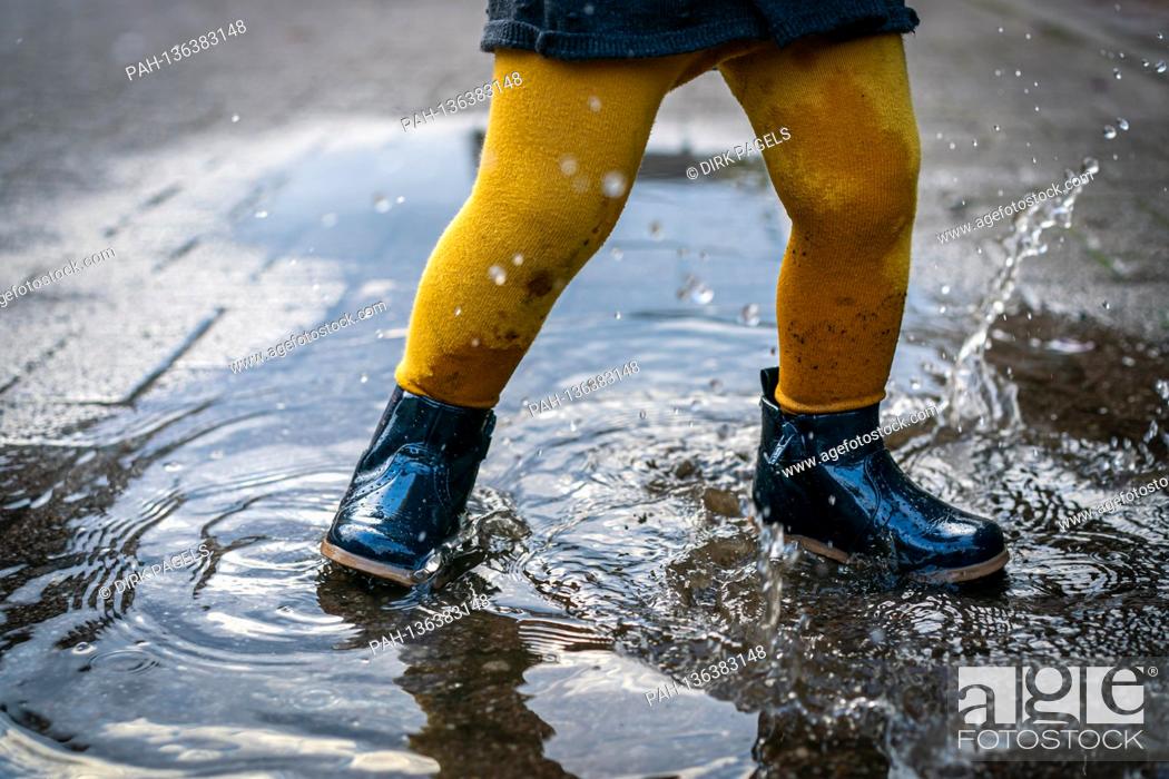 Stock Photo: October 7th, 2020, Trebbin, a little girl with rubber shoes and yellow tights jumps around in a puddle and has a lot of fun. | usage worldwide.