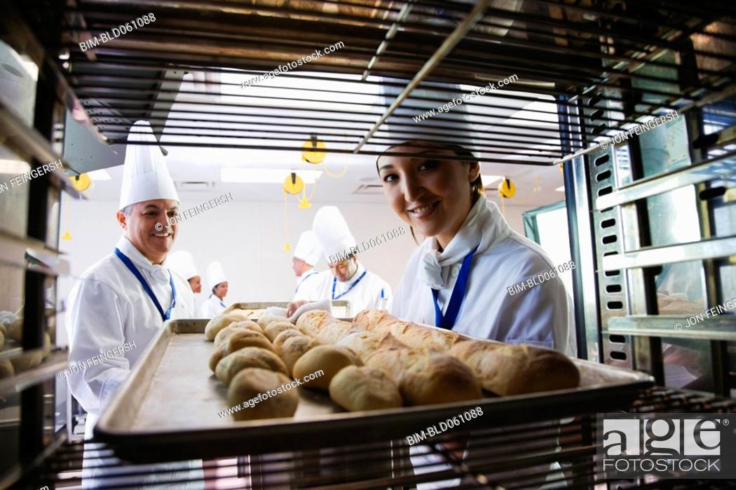 Stock Photo: Asian female baker taking tray of bread off rack.