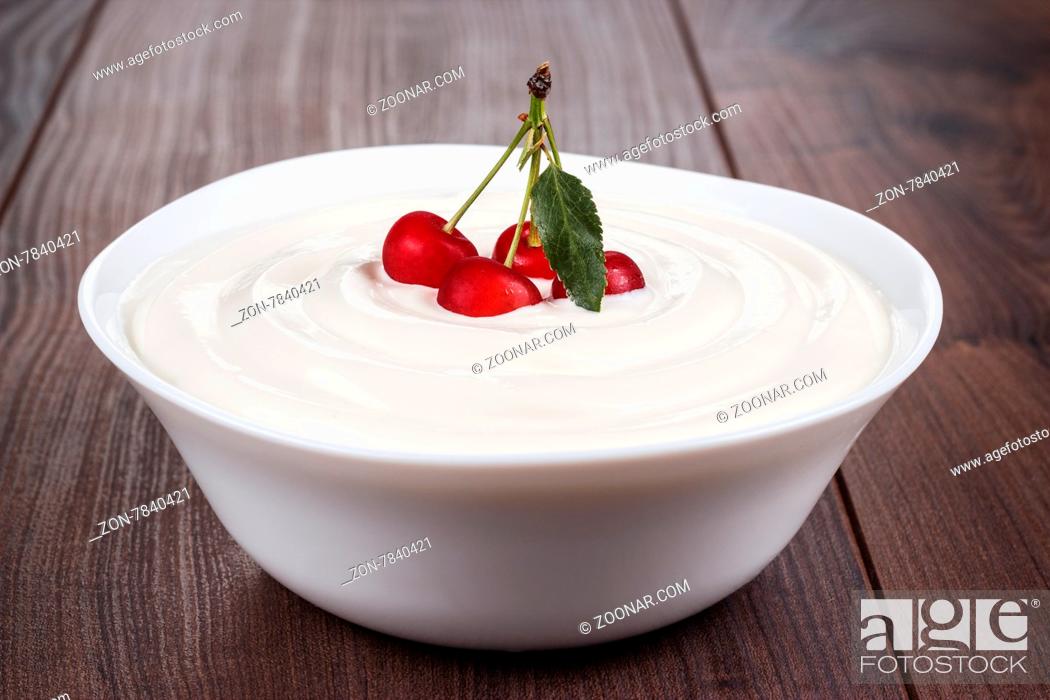 Stock Photo: white bowl full of sour cream with some cherries on top.