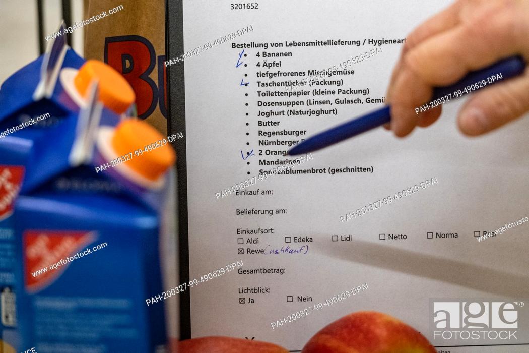Stock Photo: 26 March 2020, Bavaria, Deggendorf: ""Order of food delivery"" is on a shopping list. A helper gets food for the elderly and sick.