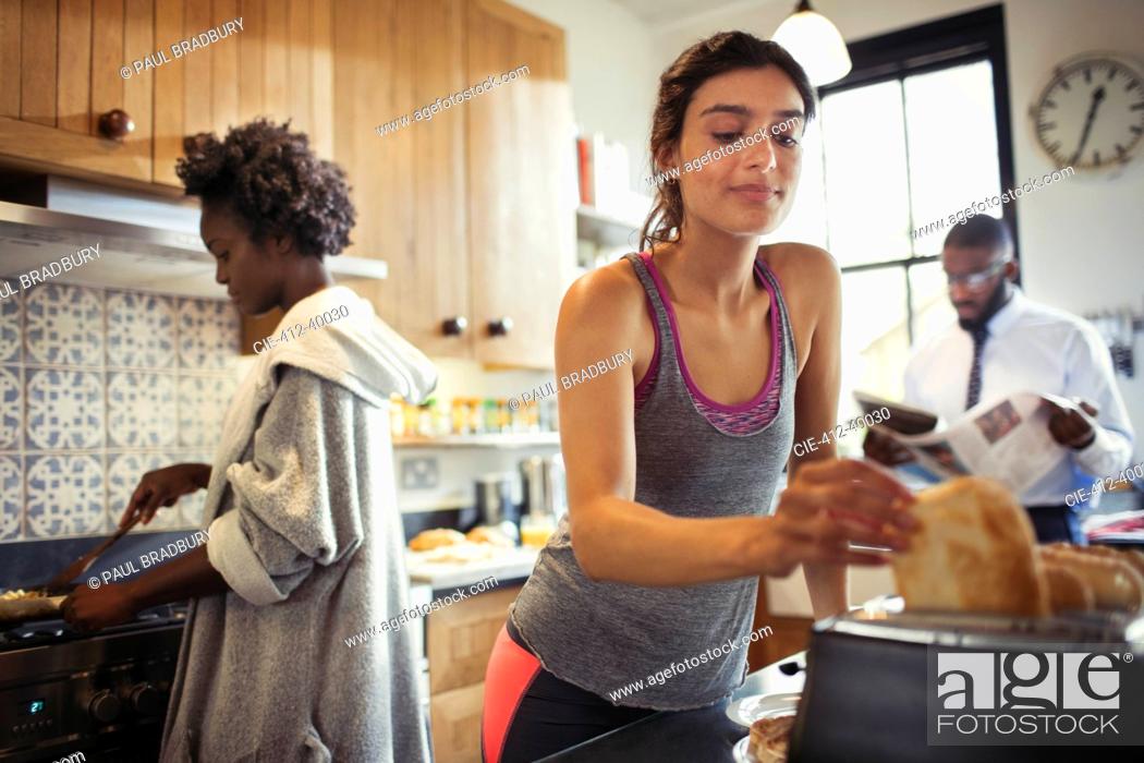 Stock Photo: Woman toasting bread in toaster in kitchen.