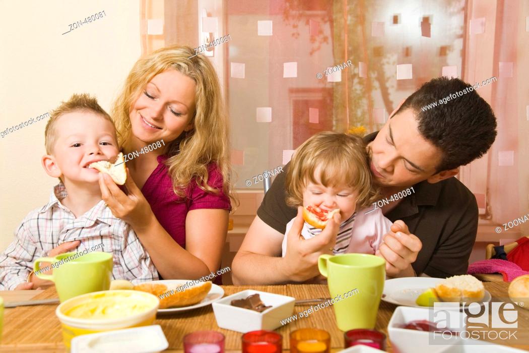 Stock Photo: Junges Ehepaar mit zwei Kindern auf dem Schoss frühstückt gemeinsam.