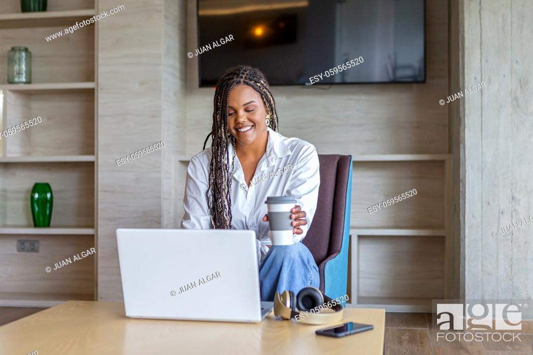 Photo de stock: African American woman using laptop in home while drinking coffee sitting. Concept of people in home.