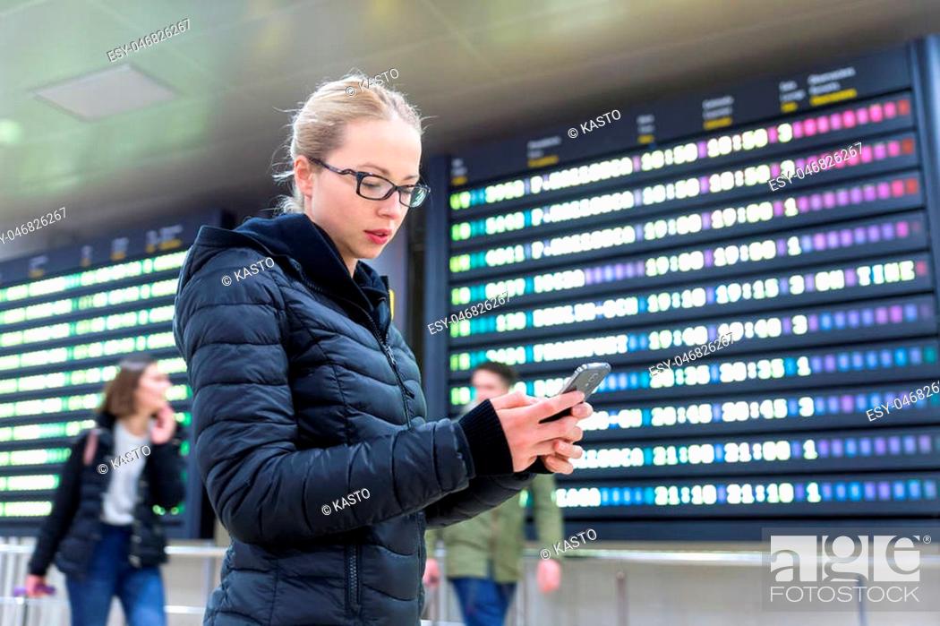 Stock Photo: Woman in international airport looking at smart phone app information and flight information board, checking her flight detailes.