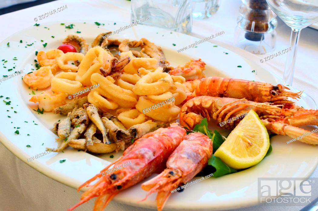 Stock Photo: Shrimps squids and other seafood on a white ceramic plate in an Italian restaurant. Food photo in the style of snapshot.