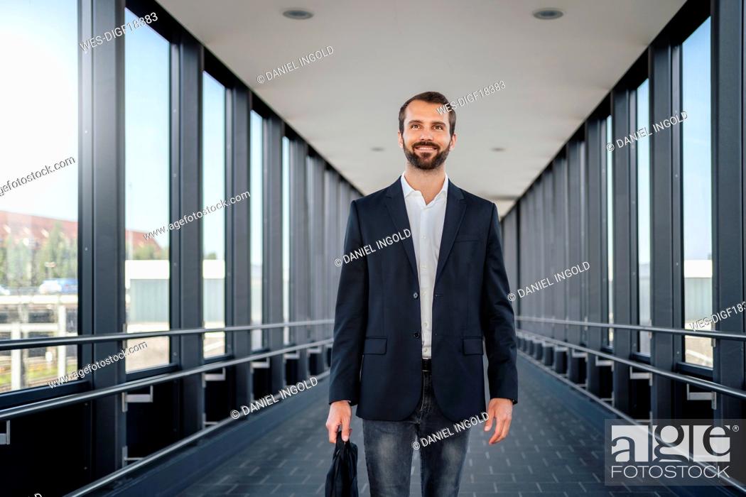 Stock Photo: Smiling businessman with bag walking on elevated walkway.