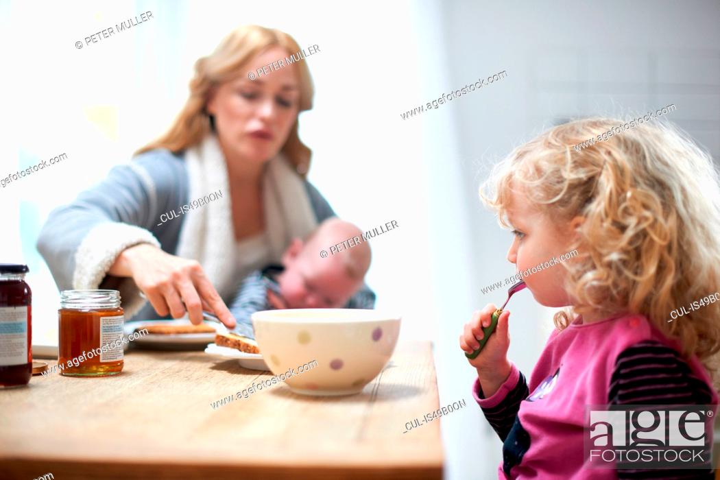 Stock Photo: Mother holding baby boy, sitting at kitchen table with young daughter, having breakfast.