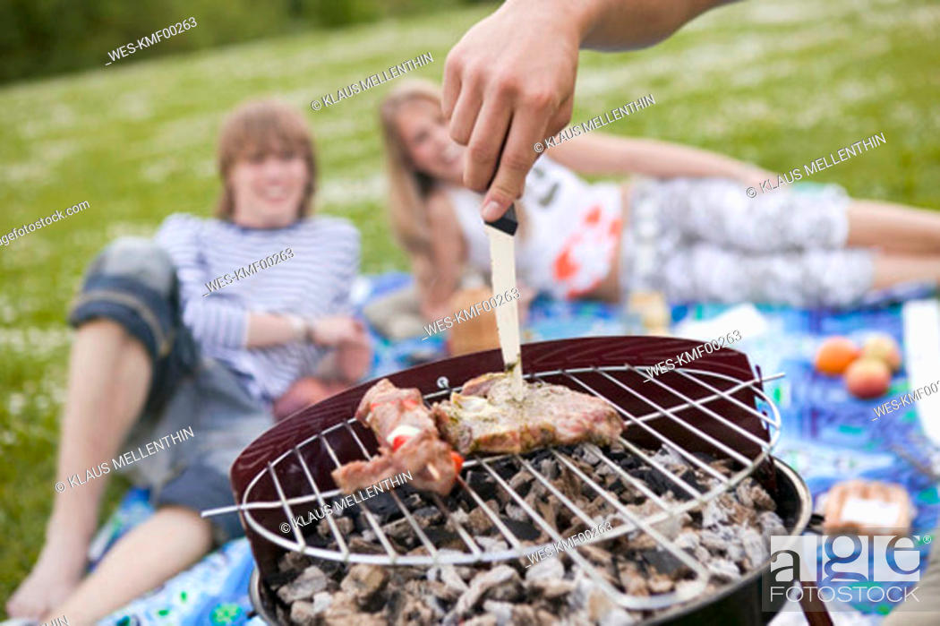 Stock Photo: Meat on grill, teenagers in background.