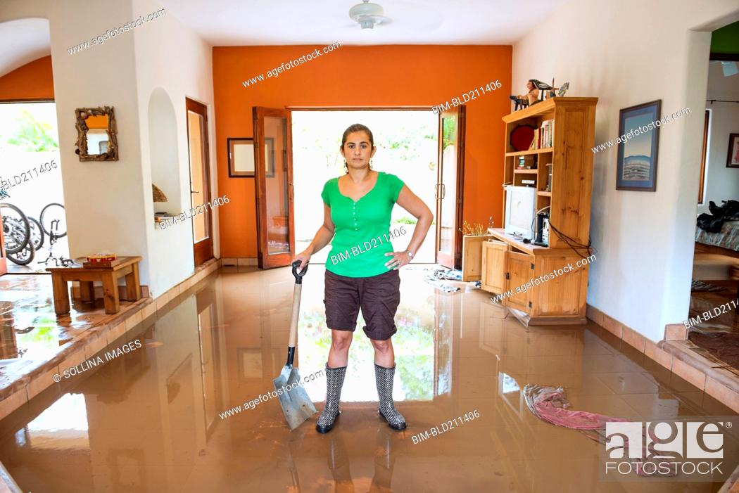 Stock Photo: Hispanic woman shoveling water out of flooded house.