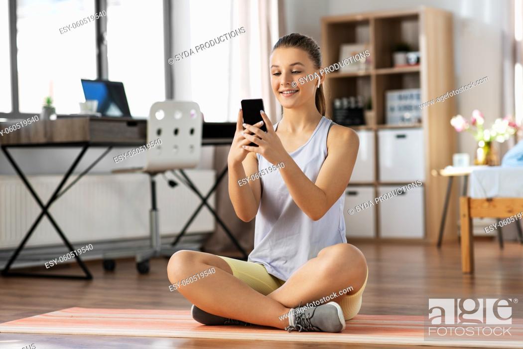 Stock Photo: girl with phone and earphones exercising at home.