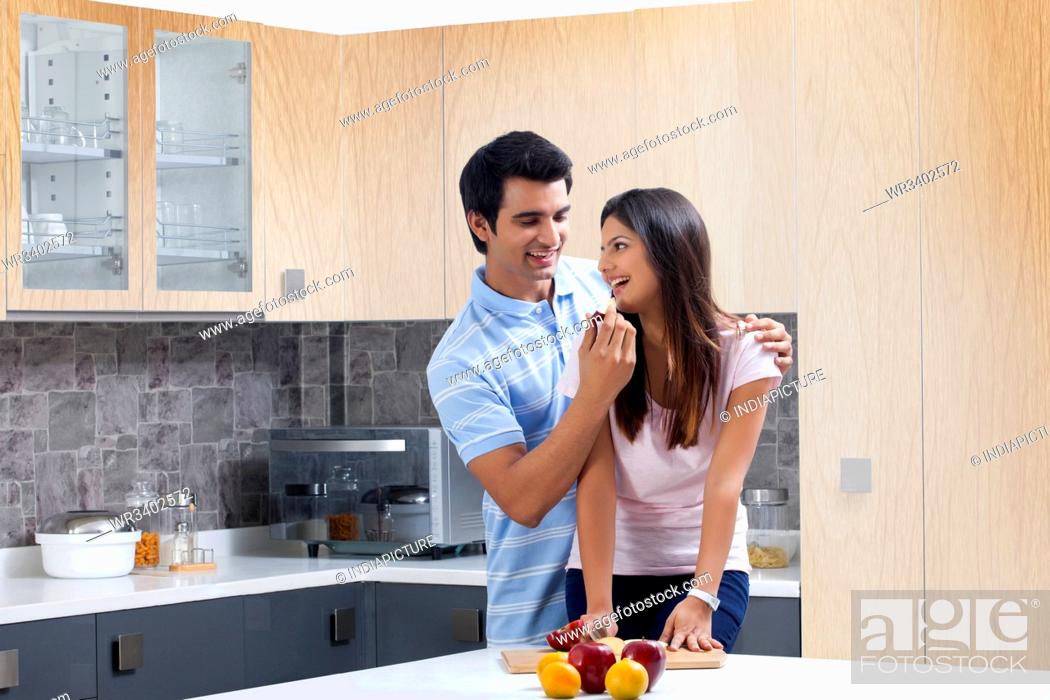 Stock Photo: Smiling man feeding fresh apple to woman in kitchen.