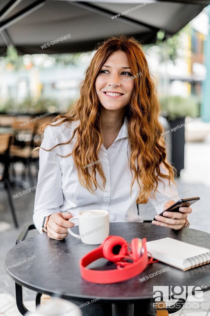 Stock Photo: Young businesswoman sitting in cafe, using smartphone.