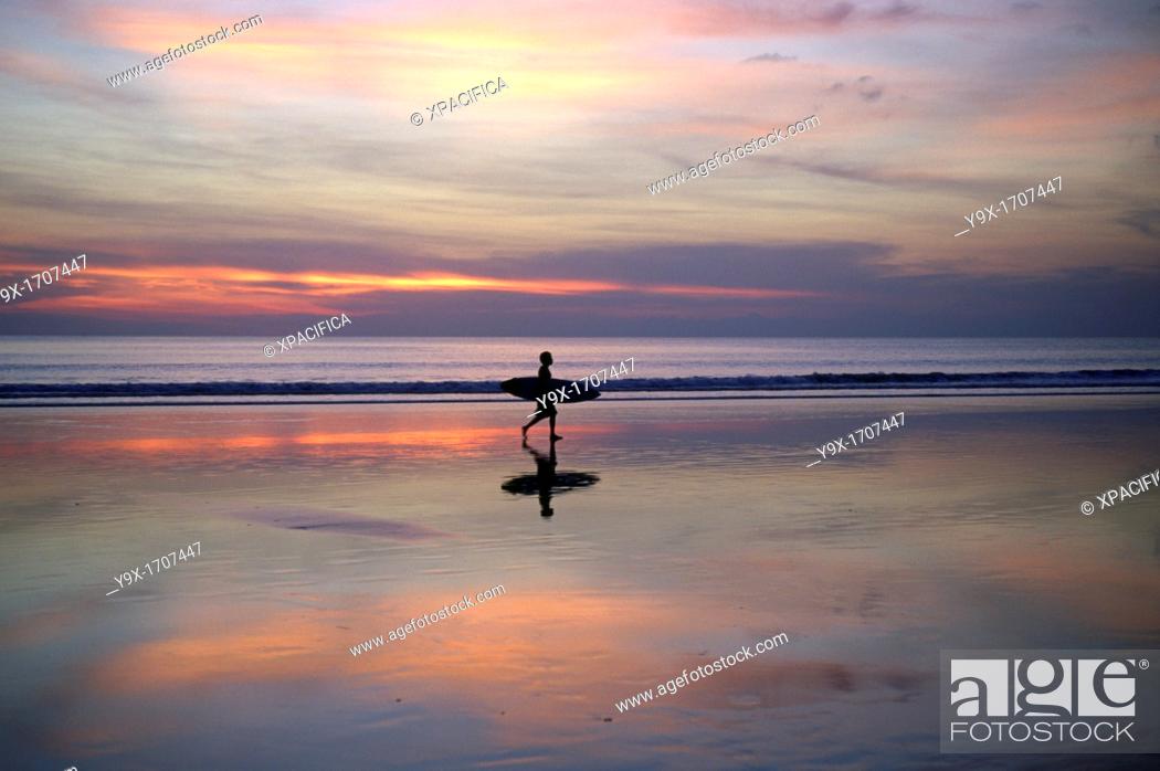 Stock Photo: Sunset on Kuta Beach, surfers carry their surfboards from the ocean after a long day riding the waves.