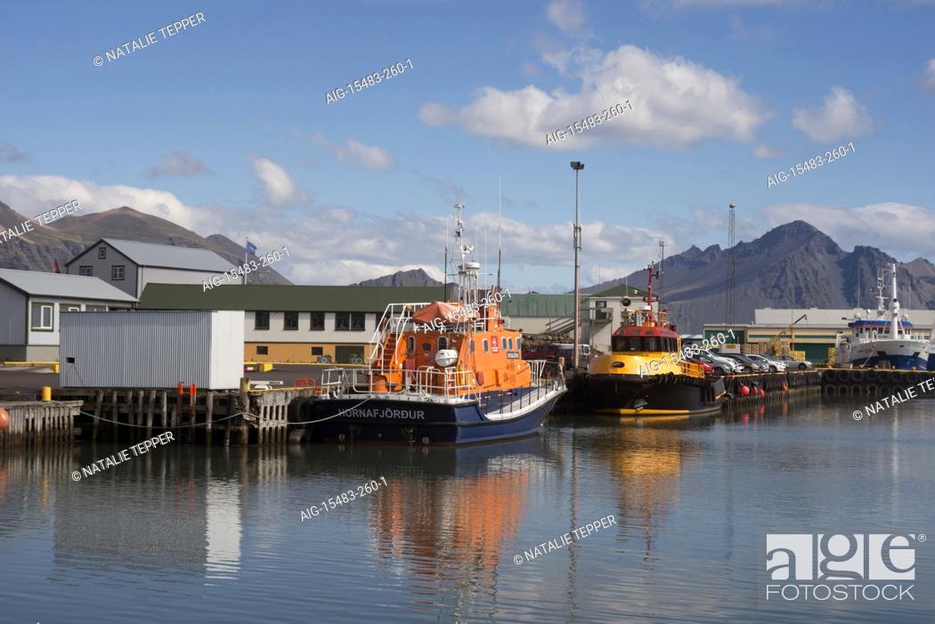 Stock Photo: A busy fishing harbour in Hofn, Iceland, with boats moored outside the dock and mountains in the background.