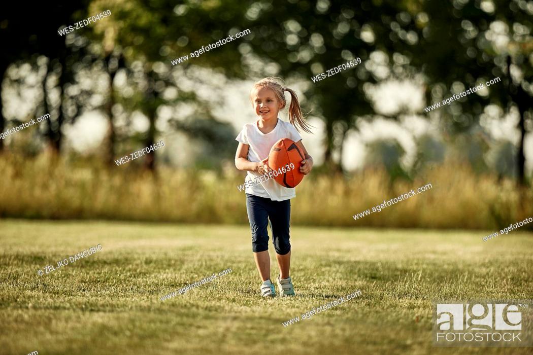 Stock Photo: Smiling girl with rugby ball walking at sports field.