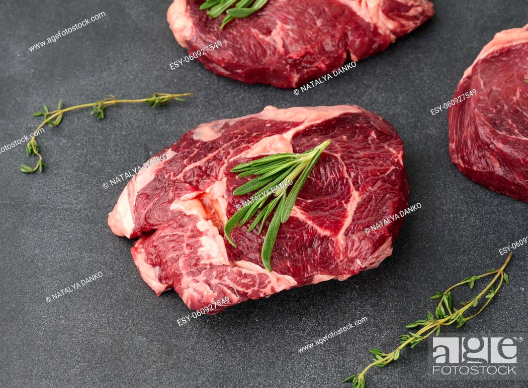 Stock Photo: raw piece of beef ribeye with rosemary, thyme on a black table, top view.