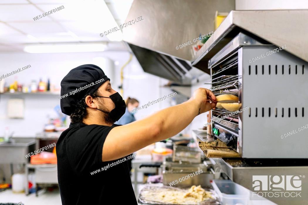 Stock Photo: Male chef preparing bread in oven at restaurant kitchen during COVID-19.