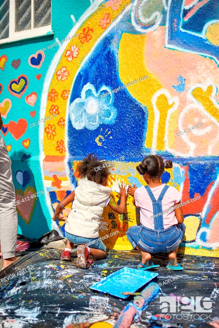 Stock Photo: Girls painting vibrant mural on sunny wall.