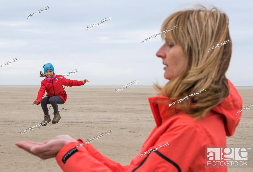 Stock Photo: Seemingly, a little girl jumps from her mothers hands into the air at the beach on the Danish island Römö, Denmark, 12 May 2015.