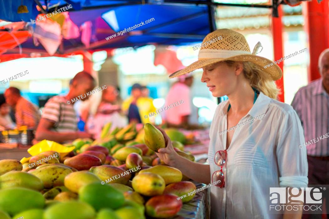 Stock Photo: Female traveler wearing elegant colonial style white tunic and hat buying fresh tropical fruit on traditional Victoria food market on Seychelles islands.
