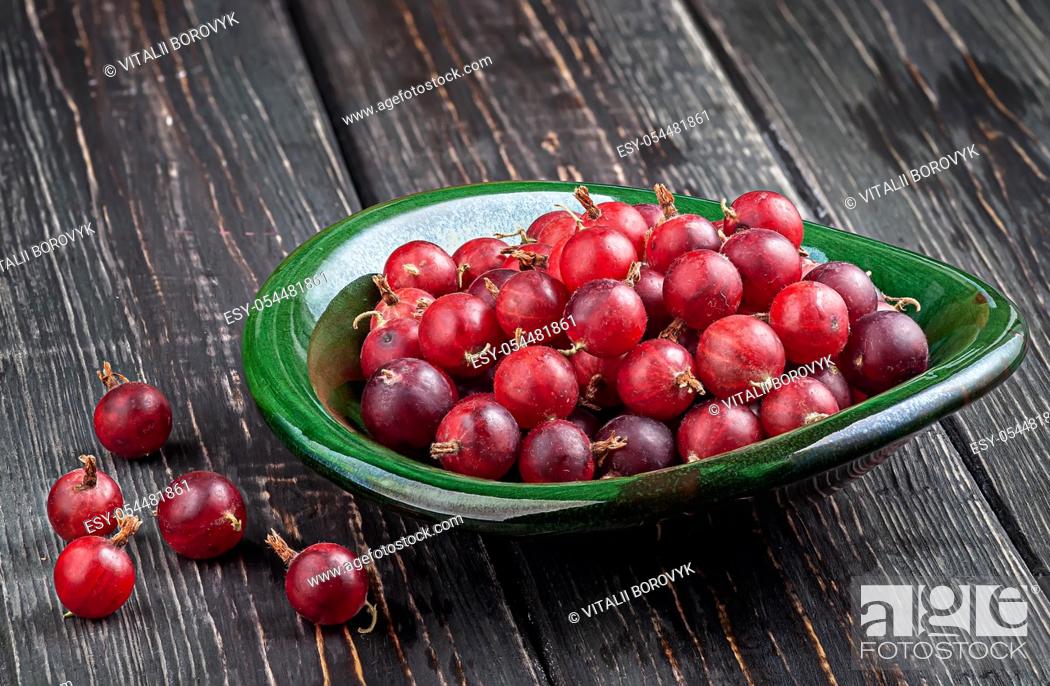 Imagen: Red gooseberries on a dark table in a clay bowl.
