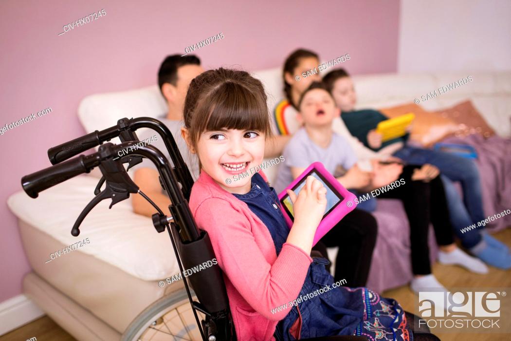 Stock Photo: Happy young girl in wheelchair using digital tablet.