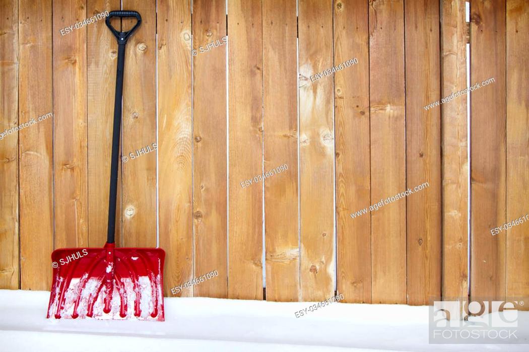 Stock Photo: Red snow shovel leaning up against a fence on a snow drift.