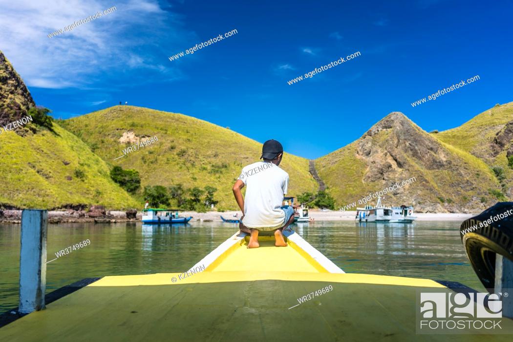 Stock Photo: Rear view of a young man enjoying the tranquil view of Padar Island, while sitting on a jetty in a sunny day during summer vacation in Indonesia.