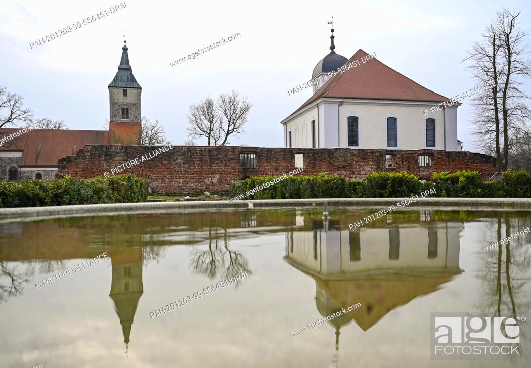 Stock Photo: 01 December 2020, Brandenburg, Altlandsberg: The town church (l) and the castle church are reflected in the water of a fountain on the grounds of the former.