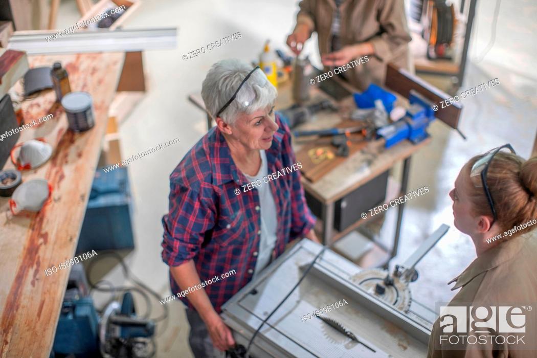 Stock Photo: Female carpenter showing equipment to trainee in furniture making workshop.