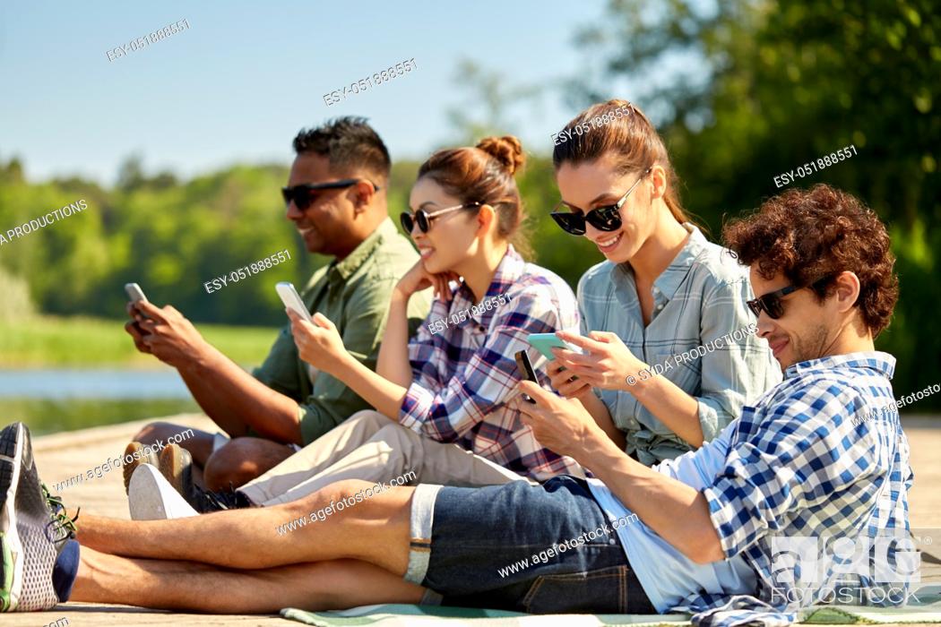 Stock Photo: friends with smartphone on lake pier in summer.