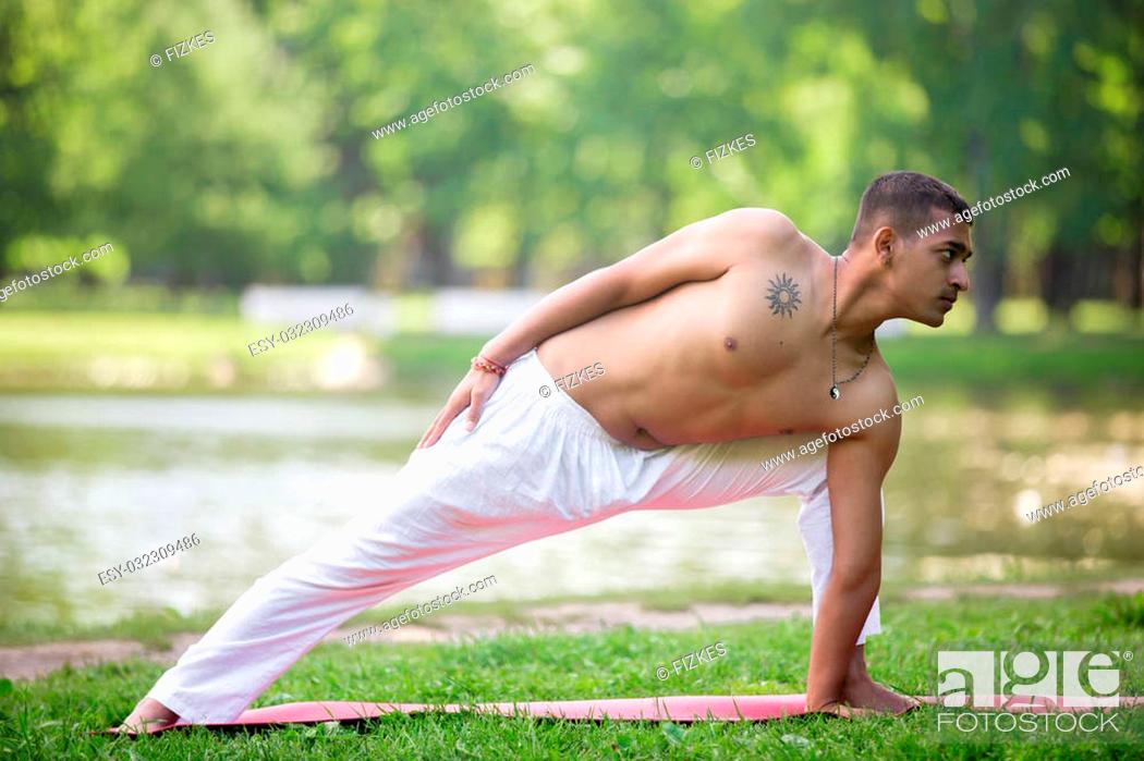 Stock Photo: Sporty asian young man in white sportswear working out on grass in park, doing yoga, fitness, pilates training, doing low lunge exercise, anjaneyasana variation.