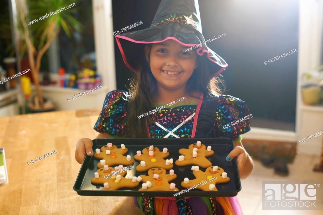 Stock Photo: Girl wearing halloween witch costume holding tray of gingerbread men.