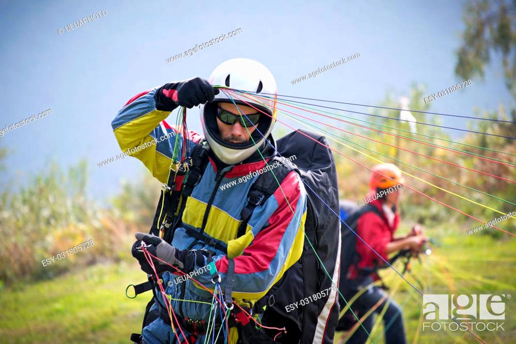 Stock Photo: paraglider pilot preparing for lift-off in reverse launch style. Wearing his helmet and gloves, tightly pulls the multi-colored strings.