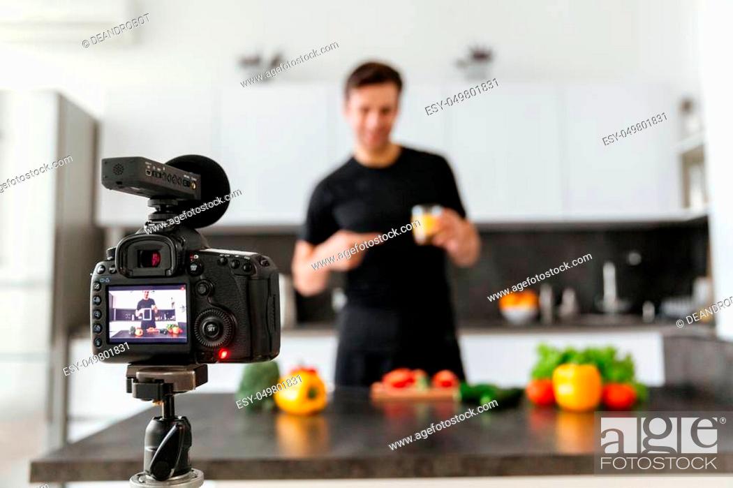Stock Photo: Close up of a video camera filming smiling male blogger cooking at the kitchen.