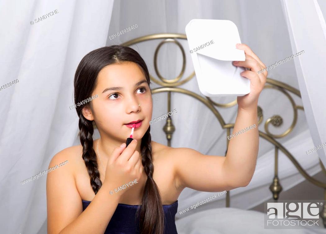 Stock Photo: little girl sitting on a bed looks in the mirror and painting lips like her mom.