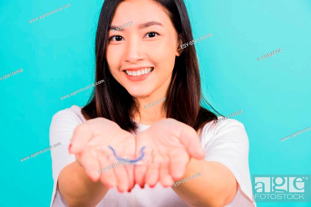 Stock Photo: Portrait young Asian beautiful woman smiling holding silicone orthodontic retainers for teeth on hand palm, Teeth retaining tools after removable braces.